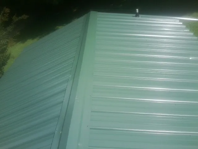 New green metal panels meeting at the ridge of a roof — Flat Roof Repair work by our crew in Colchester