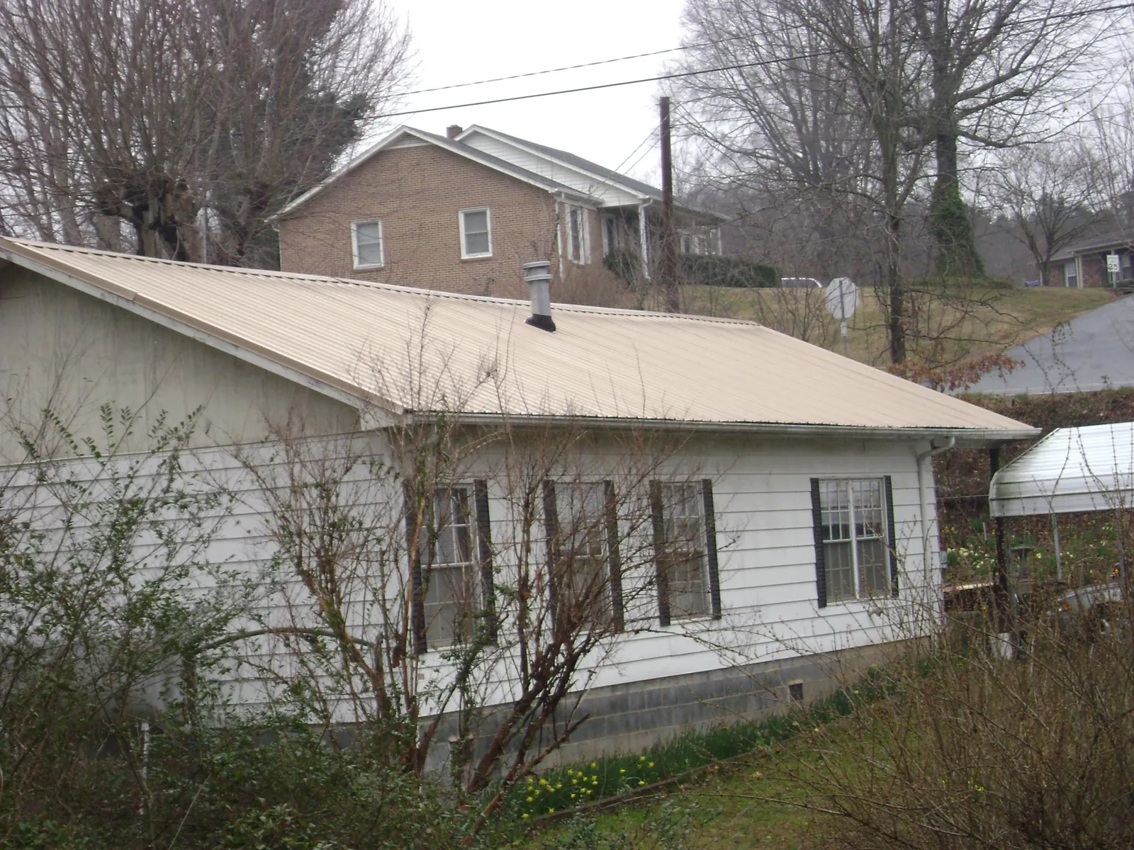 Tan metal roof on a white sided house set into a hillside — Commercial Roofing by Roofing Brothers in Colchester