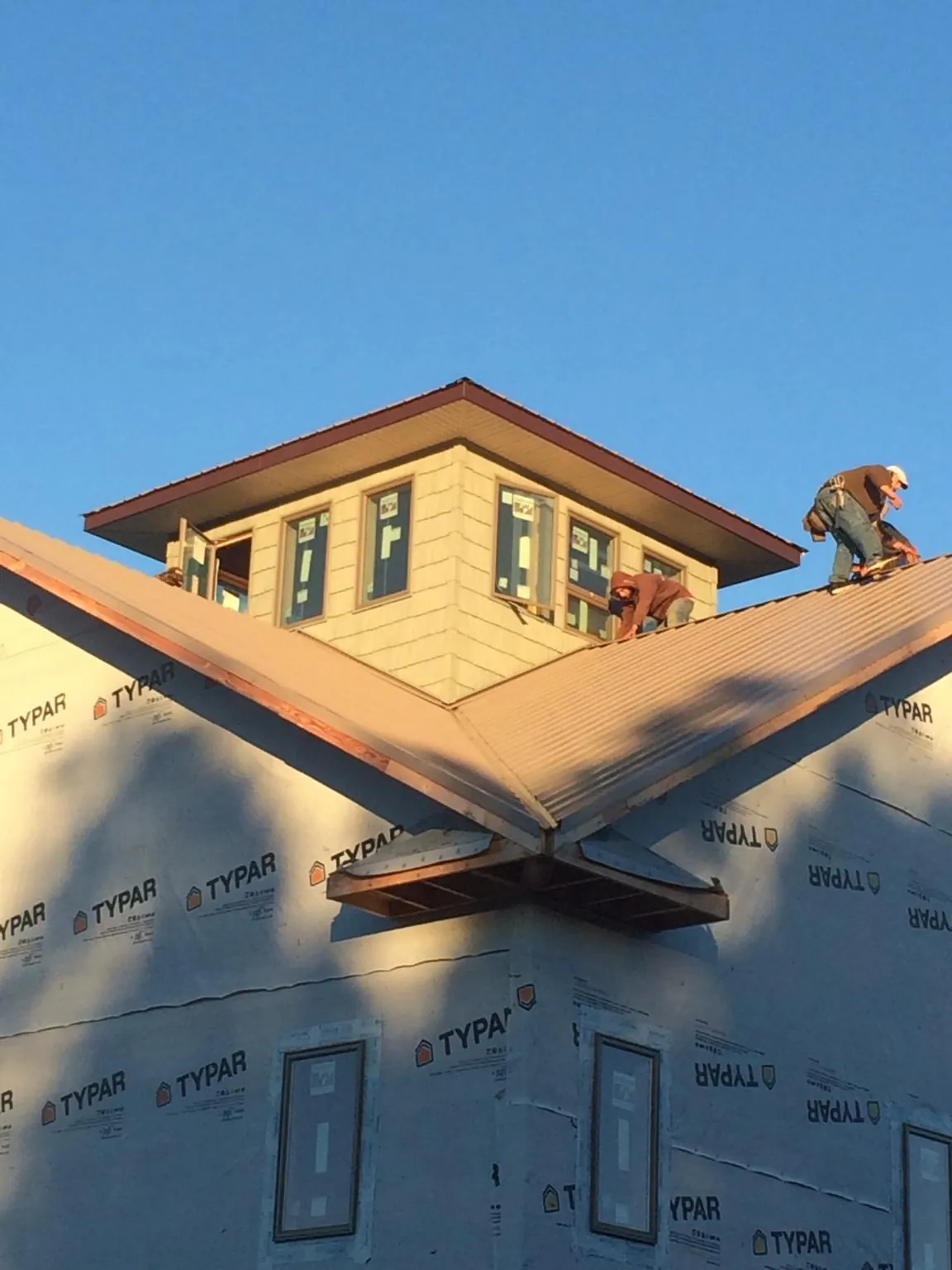 Roofers working around a rooftop cupola on a new metal roof at sunset — Roof Waterproofing in Colchester by Roofing Brothers